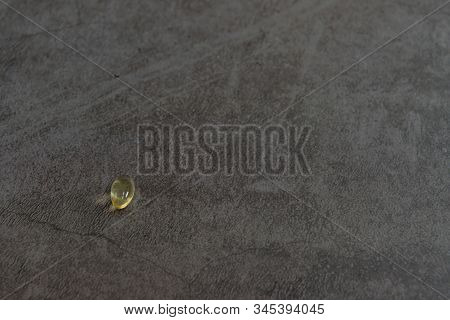 One Single Vitamin D Capsules Isolated On Black Textured Background.