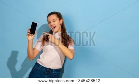Showing Phone Screen, Pointing. Caucasian Teen Girls Portrait On Blue Background. Beautiful Model In