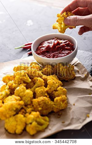 Close Up Hand Dips Cauliflower In Tomato Sauce On Black Background