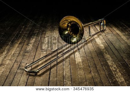 Golden Brass Instrument Trombone Lies On A Brown Wooden Stage