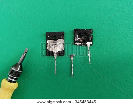Damaged Broken Bipolar Transistor With A Small Screwdriver On A Green Background