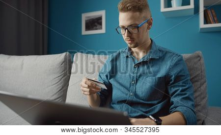 Casual Young Man Doing Online Purchase By Credit Card Using Laptop Staying Home