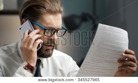 Portrait Of Bearded Businessman In Eyeglasses Holding And Looking At Document While Talking On Phone