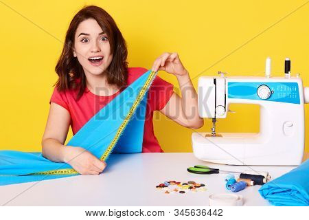 Horizontalshot Of Happy Astonished Woman Dressmaking With Sewing Machine, Using Measure Tape, Sewing