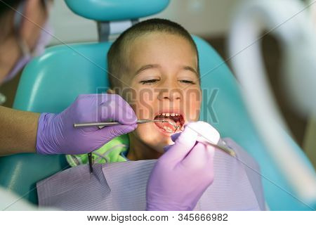 Pediatric Dentist Examining A Little Boys Teeth In The Dentists Chair At The Dental Clinic. A Child 