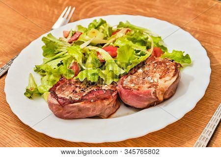 Tasty Pork Tenderloin Meat Steak In Dried Ham With Salad With Sloced Tomato And Cucumber On White Pl
