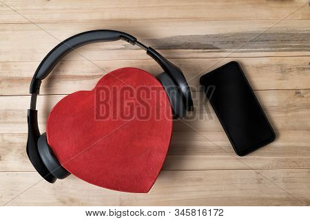 Full-size Wireless Headphones Pulled Over Red Heart-shaped Box And Smartphone On Light Brown Wooden 