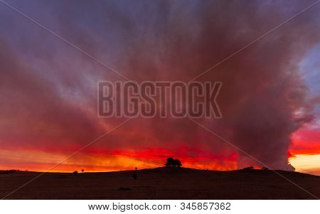 Looking Back Over Farmlands And Rural Fields To The Bush Fire Near Braidwood, Australia At Dusk.