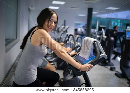 Woman training in a gym using a stationaty bike, cardio and stamina workout concept