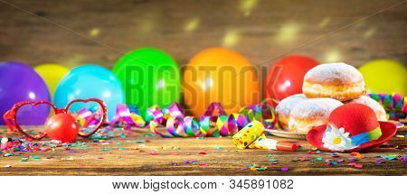 Krapfen, berliner or donuts with bow tie, party hat, streamers, confetti and balloons. Colorful party, carnival or birthday background