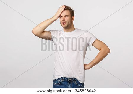 Focused And Thoughtful Young Handsome Blond Bearded Male In White T-shirt, Punch Forehead, Squinting