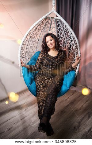 Fat Plump Charming Cute Woman With Black Curly Hair In Black Beautiful Dress In A White Wicker Chair
