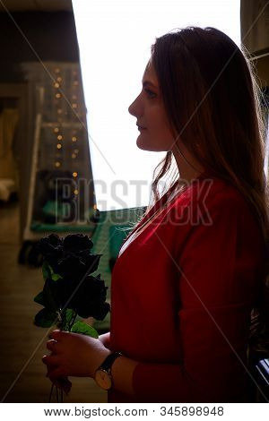 Girl In Red Costume With Black Rose On Her Hand Near Mirrow In The Dark Room
