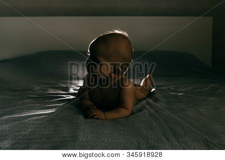 A Child Naked Lie On Bed In The Dark In A Counterlight.