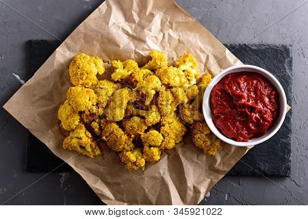 Top View Of Yellow Cauliflower In Crispy Batter With Tomato Sauce On Kraft Paper On Black Background