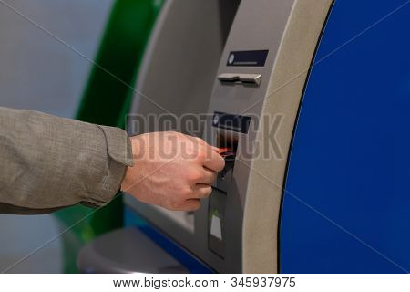A Male Hand Inserts A Credit Card Into An Atm. Hole For A Plastic Card. Man Withdraws Cash Through A