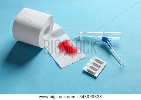 Anoscope, Suppositories And Toilet Paper With Red Feather On Light Blue Background. Hemorrhoid Treat