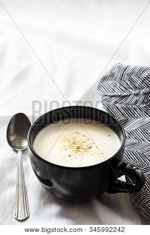 Cauliflower Soup (creme Du Barry) In Black Bowl On White Background With Black And White Cloth.