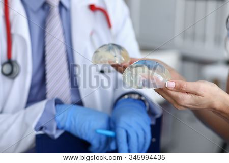 Close-up Of Female Hands Holding Silicone Implants In Hands. Plastic Surgeon In Medical Gown Advisin