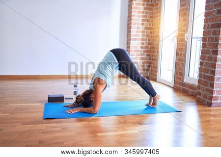 Middle age beautiful sportwoman standing on mat practicing yoga doing dolphin pose at gym