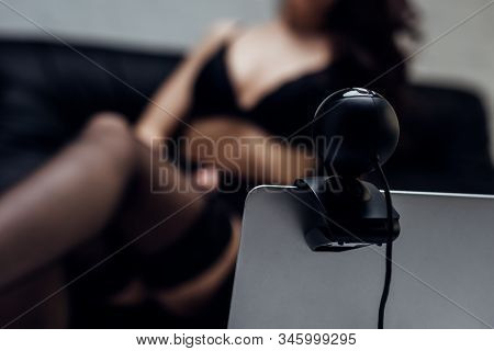 Selective Focus Of Laptop With Web Camera And Girl In Bra And Stockings On Sofa