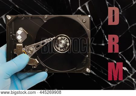 Man In Blue Latex Glove Holds Hard Drive With Abbreviation (drm) Digital Rights Management On Dark B