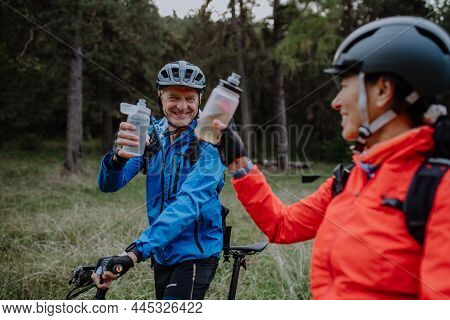 Happy Senior Couple Bikers With Wtaer Bottles Outdoors In Forest In Autumn Day.