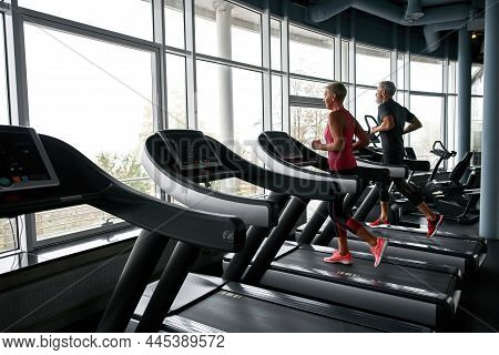 Healthy Seniors Running On Treadmills In Gym. Fit Couple Training Together To Practice Self-care And
