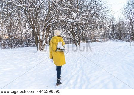 Young Woman In Yellow Jacket With Ice Skates Walking Through Snowy Park