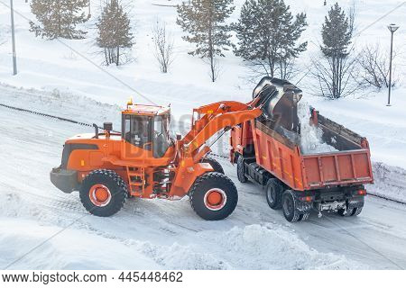 Big Orange Tractor Cleans Up Snow From The Road And Loads It Into The Truck. Cleaning And Cleaning O