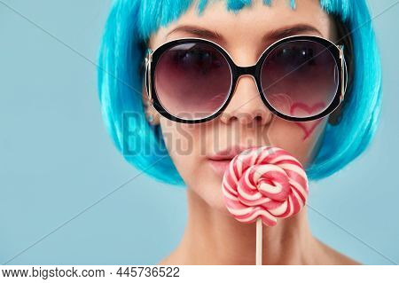 Young Funky Girl In Blue Wig And Eyeglasses, Holding Lollipop Candy, Looking Aside With Dreamful Smi