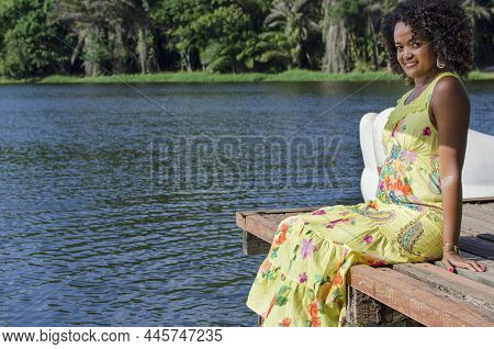 Portrait Of A Beautiful Black Woman Sitting On The Pier Of A Lake