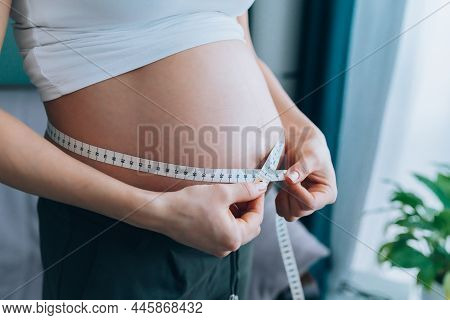 Close-up Of Torso Of Unrecognisable Pregnant Woman In White T-shirt Measuring Her Growing Abdomen Si