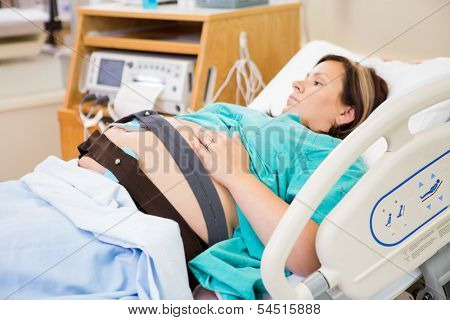 Mid adult pregnant woman with ctg monitor on belly