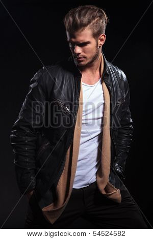 side view of a fashion man in leather jacket is looking to his back on dark background