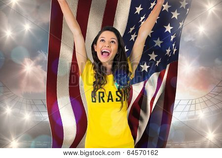 Excited football fan in brasil tshirt holding usa flag against large football stadium under cloudy blue sky