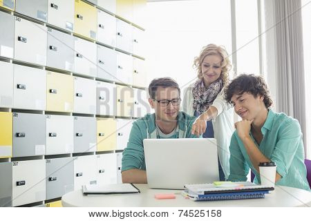 Businesspeople using laptop at table in locker room at creative office