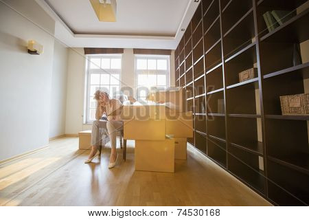 Full-length of stressed woman sitting by cardboard boxes in new house