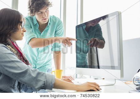 Creative businessman showing something to colleague on desktop computer in office