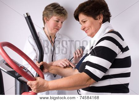 Senior is being observed by doctor after training, measuring blood pressure