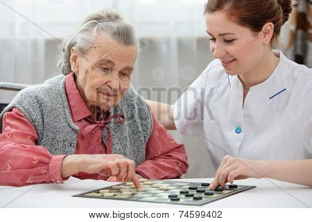 Senior woman playing checkers with a nurse in a retirement home