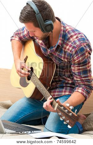 Man on sofa playing the guitar with laptop at home