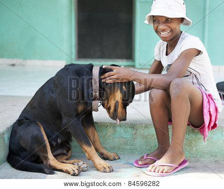 A tween Haitian girl happily petting a large black dog.  