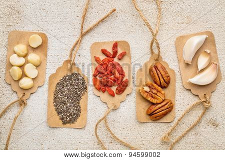 superfood abstract with price tags against barn wood (macadamia and pecan nuts, goji berries, chia seeds and garlic cloves) - healthy eating concept