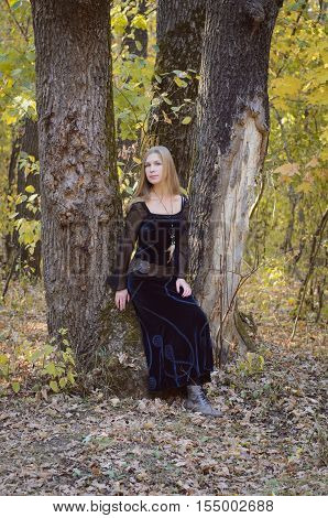 Blond Long-haired Girl In A Fantasy Black Dress In An Autumn Forest