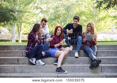 Young People Using Smartphone And Tablet Computers Outdoors