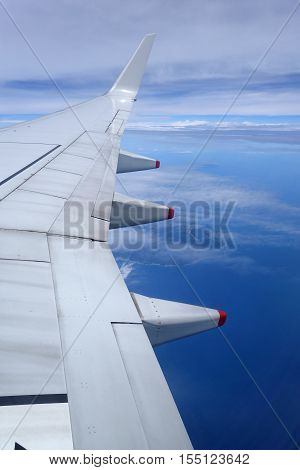 Wing of an airplane flying above the clouds on blue sky background