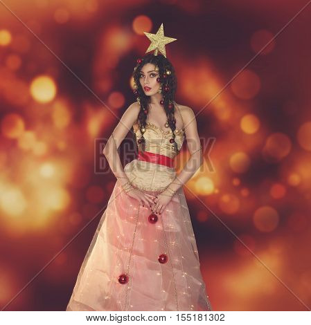 Beautiful young woman dressed like christmas tree with star on head. Studio shot on golden light background. Copy space. Sqaure composition.