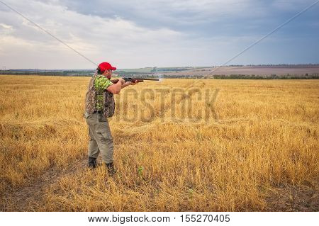 Hunter with a gun in the field aiming at the target and shoot