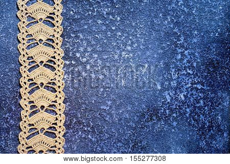 Beige crochet lace on a beautiful grunge textural dark blue cement background. Excellent background for the blog of needlework